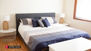 A neatly arranged bedroom with a bed, pillows, a bedside table, and a lamp. - Montaview - Mumbulla St 24 (Bermagui)
