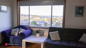 A living room with a large window, two sofas, a small table, and a potted plant. - Montaview - Mumbulla St 24 (Bermagui)