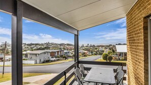 A balcony with a view of a residential area, a table, and chairs.