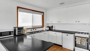 A modern kitchen with white cabinets, a black countertop, a built-in oven, and a window with a wooden frame.