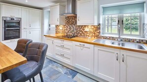 A modern kitchen with white cabinets, a tiled backsplash, and a window with a view of greenery. - Host & Stay | Kenmore (Hexham)