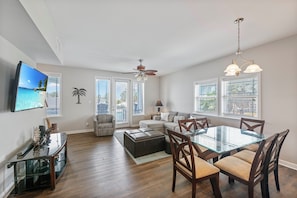 A modern living room with a glass dining table, wooden chairs, a sofa, and a ceiling fan. - Three story townhome. Garage access. Golf cart included. Very short drive to the (Port Aransas)