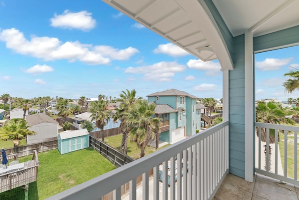 A balcony with a view of a residential area, including houses and palm trees. - Three story townhome. Garage access. Golf cart included. Very short drive to the (Port Aransas)