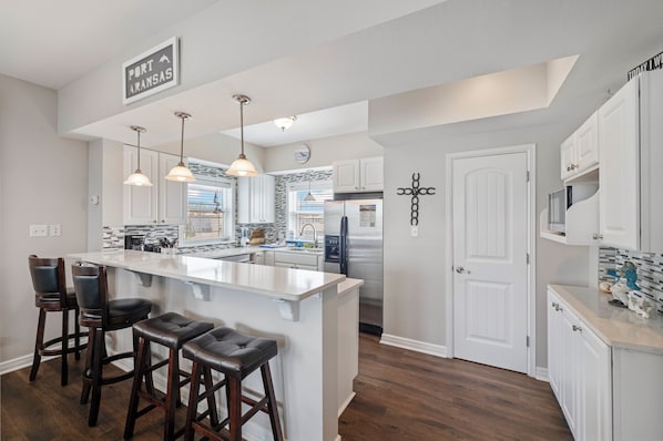 A modern kitchen with a central island, pendant lighting, and bar stools.