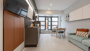 Une cuisine moderne dotée d’un four encastré, un coin repas avec une table et des chaises, et un canapé vert clair agrémenté d’un coussin à motifs.