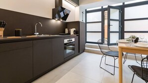 Une cuisine moderne avec des meubles de couleur sombre, un four encastré et un coin repas comprenant une table et des chaises.