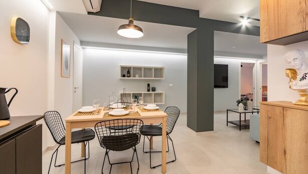 Zona pranzo moderna con tavolo in legno, sedie in filo nero e lampada a sospensione.
