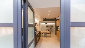 Una cucina moderna con zona pranzo, caratterizzata da un'isola centrale, illuminazione a sospensione e vista attraverso una porta in vetro.