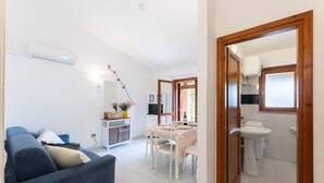 Un salon avec un canapé, une table à manger avec des chaises, un coin cuisine avec un évier et des placards, et une salle de bain avec des toilettes et un lavabo.