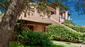 Une maison à deux étages, avec des fondations en pierre, un balcon et un jardin bien entretenu.