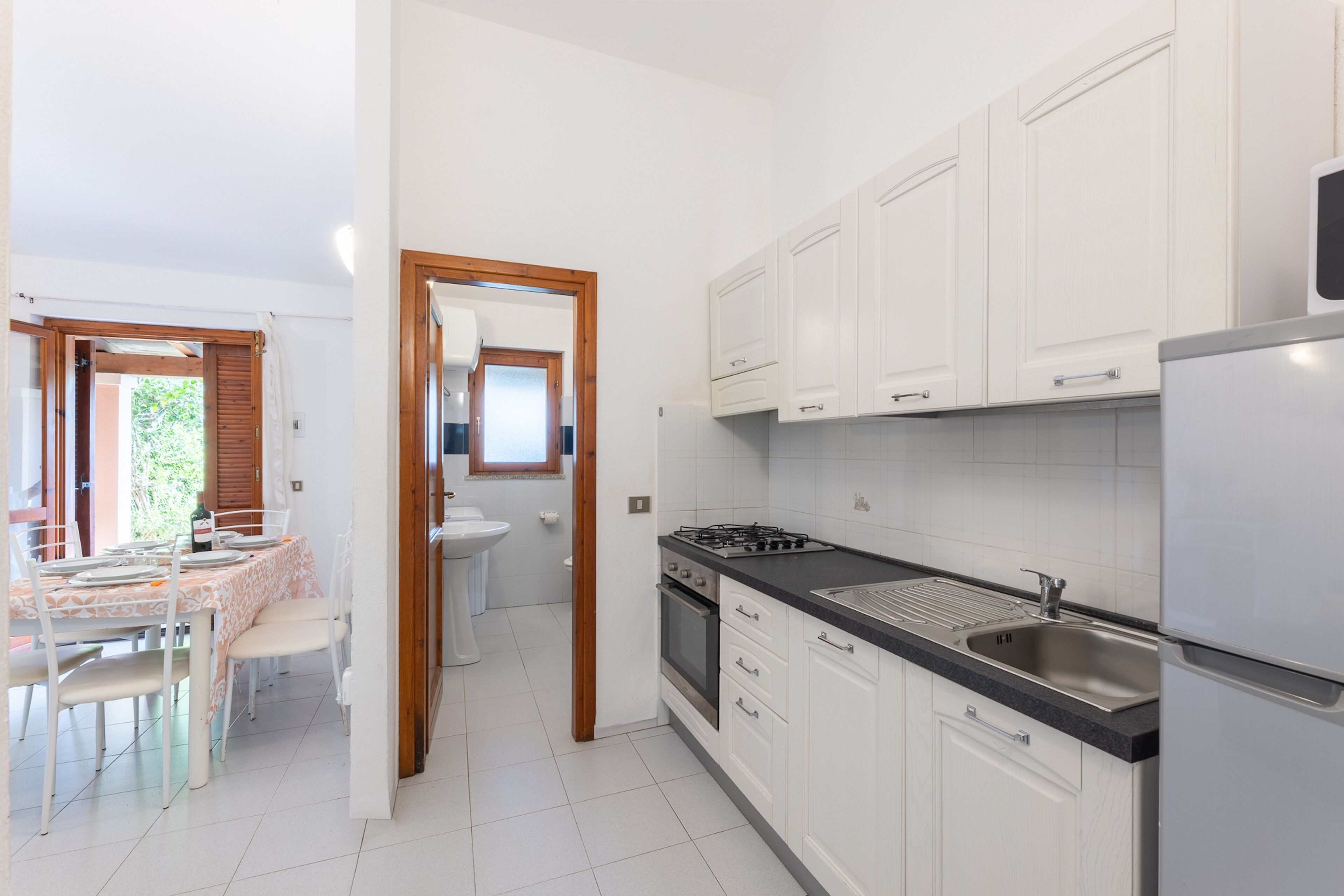 A modern kitchen with white cabinets, a stainless steel sink, and a dining area with a table and chairs.
