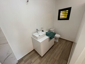A small bathroom with a white sink, toilet, and a window with blinds.