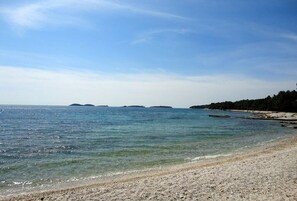 A beach with clear water, pebbly shore, and distant islands.