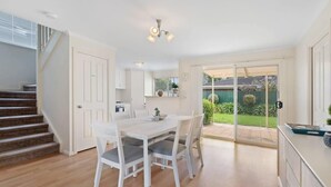 Une cuisine moderne avec un coin repas, un escalier et une porte-fenêtre coulissante donnant sur un jardin.