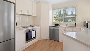 Une cuisine moderne dotée d’appareils électroménagers en acier inoxydable, de meubles blancs, d’un lave-vaisselle et d’une fenêtre avec des stores.