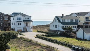 Et kystnært boligområde med huse i forskellige arkitektoniske stilarter, heriblandt et markant hvidt hus med balkon og et stenhus med veranda.