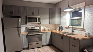 A modern kitchen with grey cabinets, stainless steel appliances, a wooden countertop, and a window with a view.