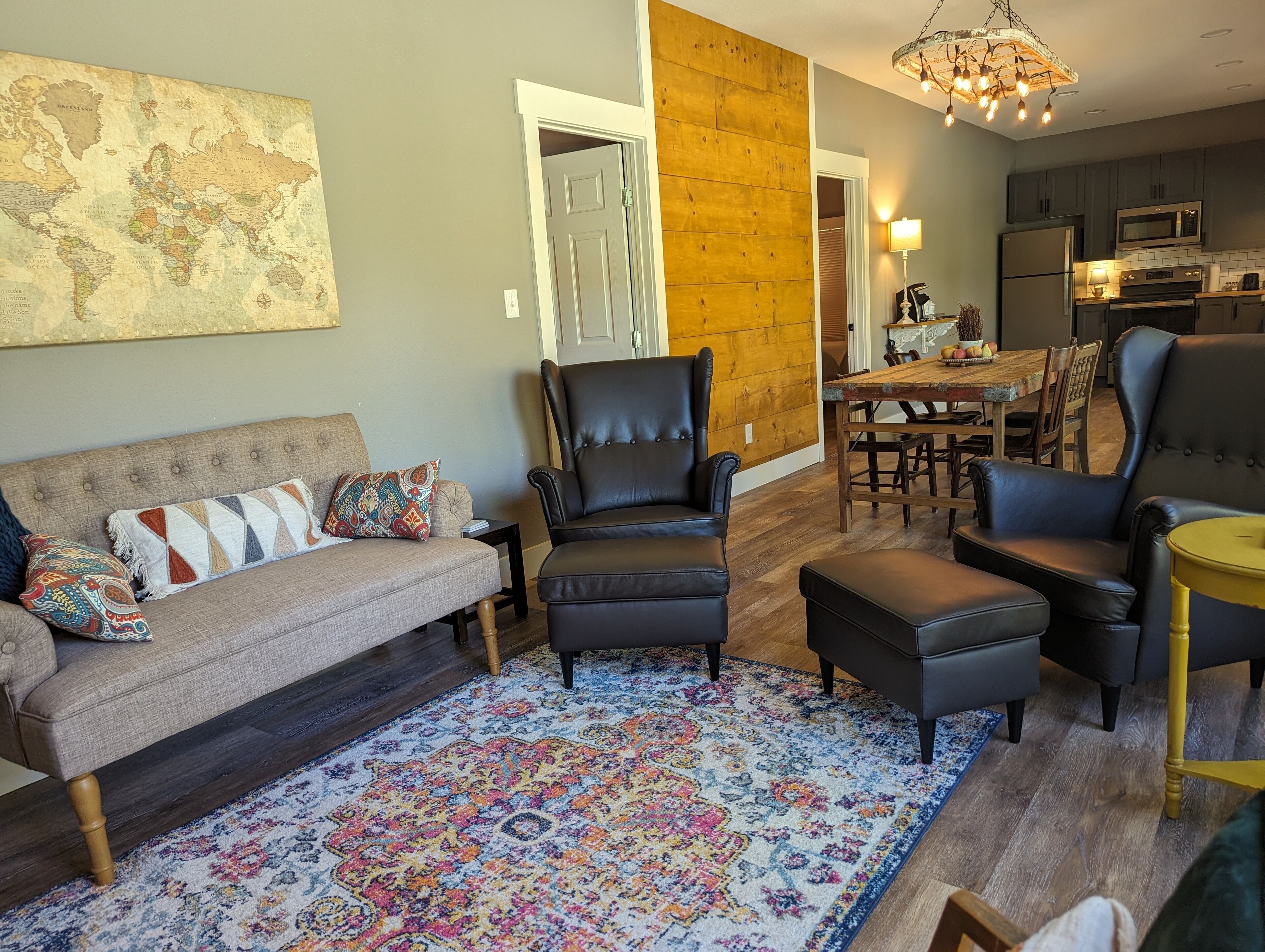 A living room with a sofa, two armchairs, a coffee table, and a rug. There is a dining table with chairs in the background.