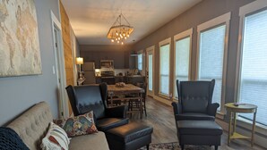 A modern living room with a sofa, two armchairs, a patterned rug, and a view of the kitchen and dining area.