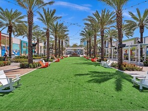 A pathway lined with palm trees and outdoor seating areas, leading to a building with a blue facade. - Two Bedroom Hollywood Beach Vacation SC01 (Hollywood)
