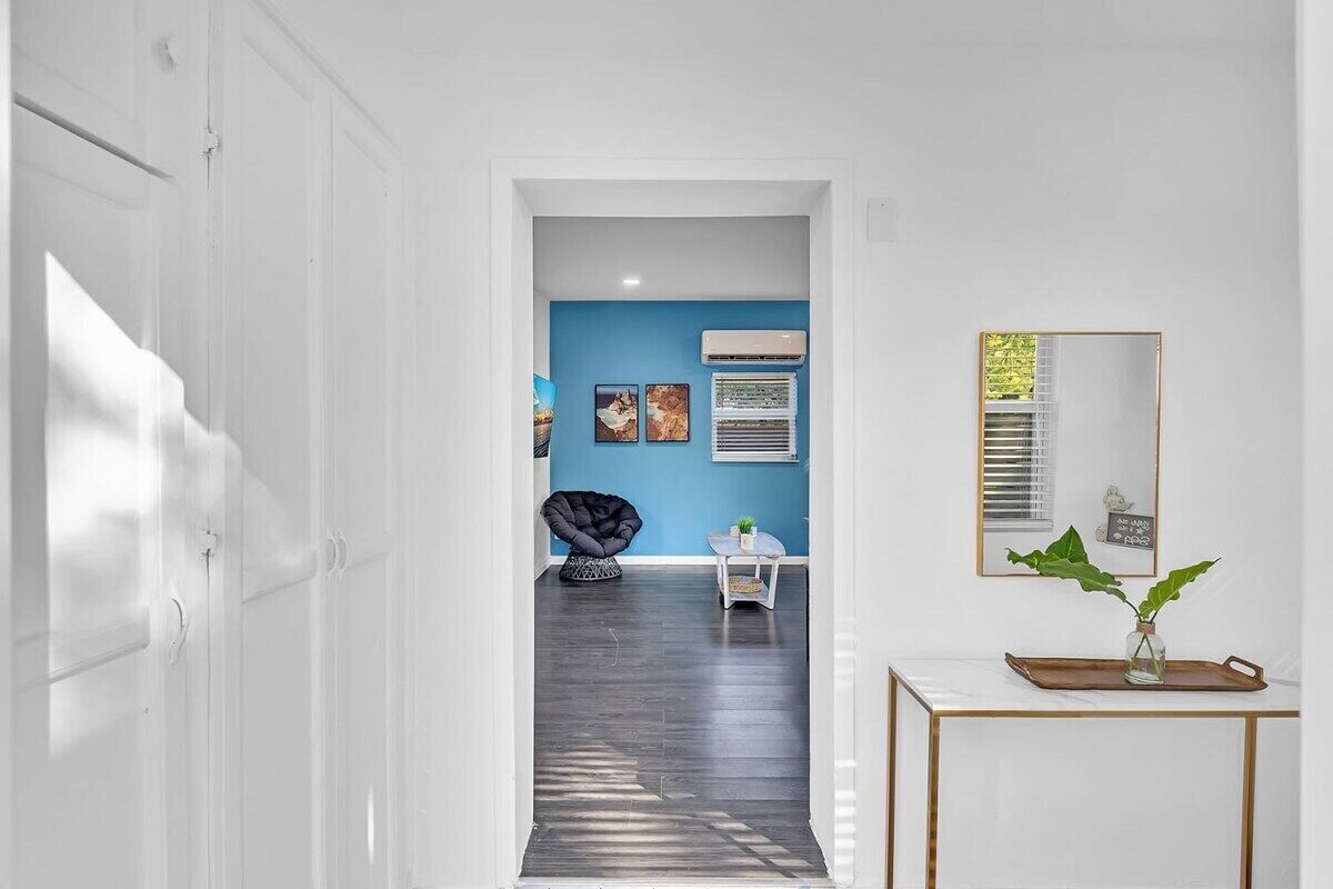 Un couloir avec un mur d’accent bleu, une chaise noire, une petite table avec une plante et un miroir posé sur une console.