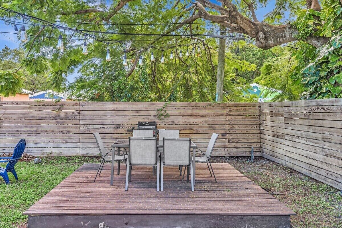 Eine Holzterrasse mit Tisch und Stühlen, umgeben von einem Holzzaun und üppiger Bepflanzung.