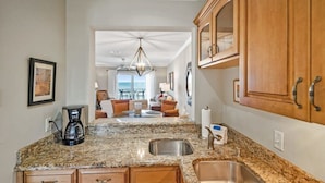 A kitchen with granite countertops, wooden cabinets, a coffee maker, and a view to a dining area with chairs and a table. - Oceanfront, Patio, Pool, Tennis, BBQ, Free Parking (St. Augustine)