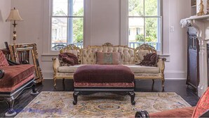 Una habitació amb una finestra gran, un sofà, un otomà, una làmpada i una llar de foc.