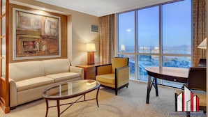 A hotel room with a large window, a sofa, a chair, a small table, and a painting on the wall. - Strip View Studio | Jacuzzi, Pool & Kitchenette (Las Vegas)