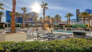 A rooftop pool area with lounge chairs, palm trees, and modern buildings in the background. - Strip View Studio | Jacuzzi, Pool & Kitchenette (Las Vegas)
