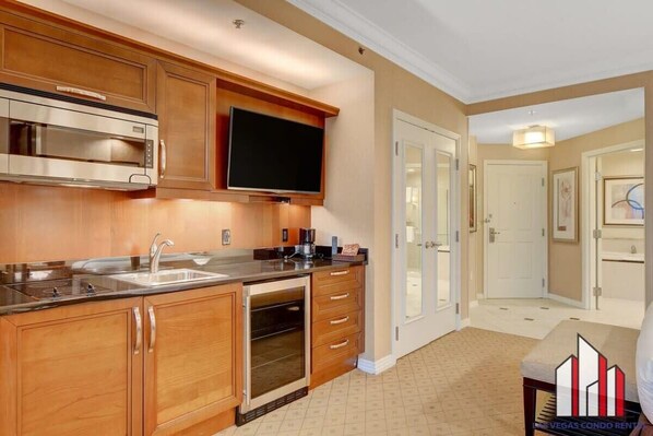 A modern kitchen with wooden cabinets, stainless steel appliances, and a flat-screen TV.