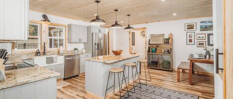 A modern kitchen with a central island, bar stools, and a patterned rug.