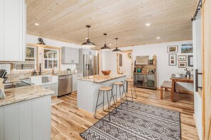 A modern kitchen with a central island, bar stools, and a patterned rug.
