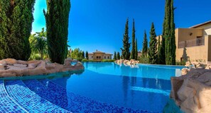 Una piscina con agua cristalina azul, rodeada de rocas y altos cipreses.