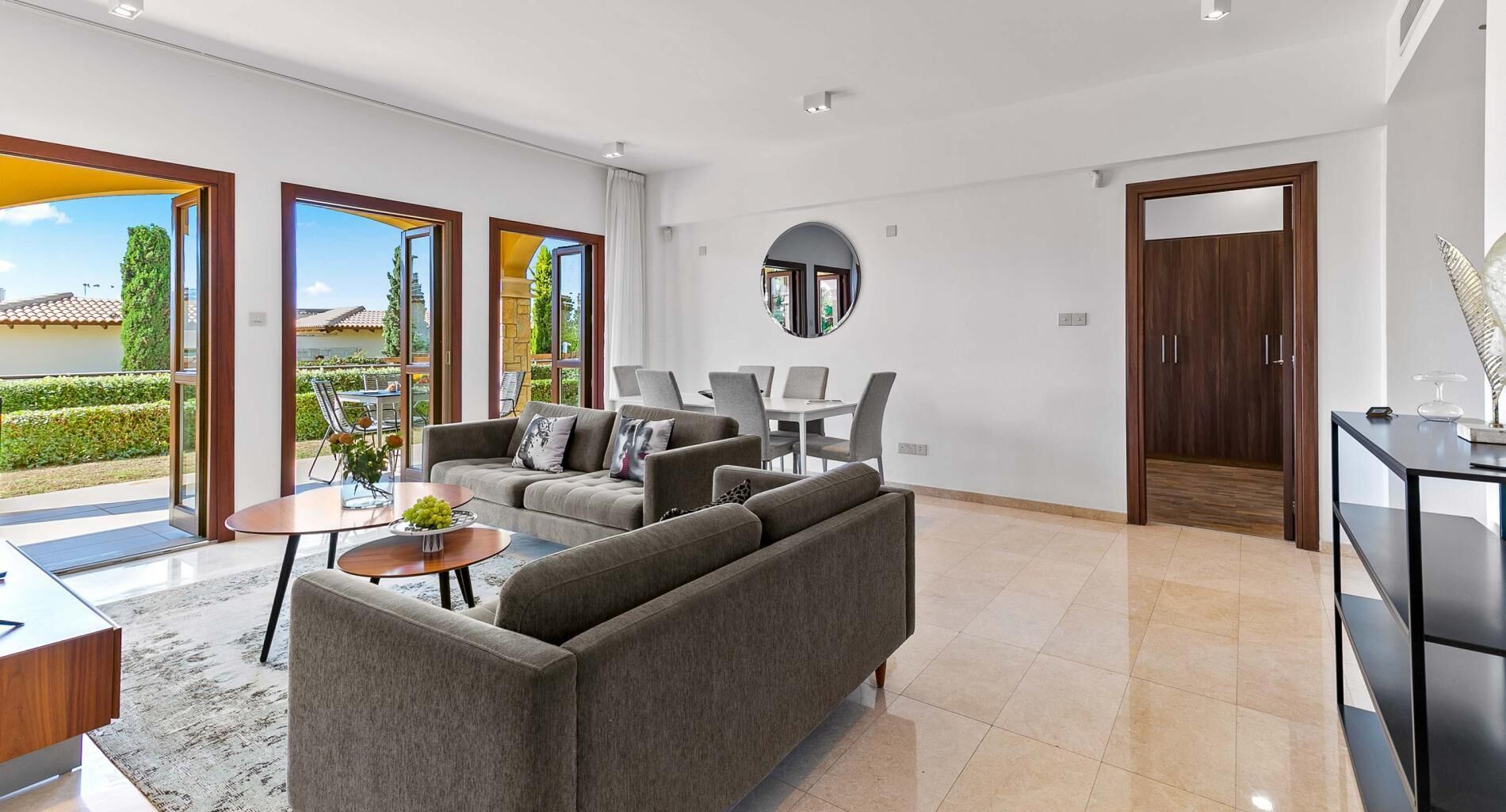 A modern living room with a grey sofa, a coffee table, and a dining area with chairs.