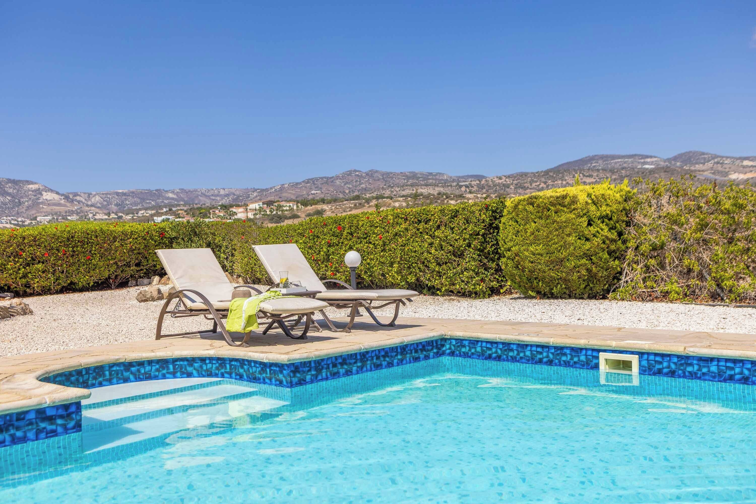 Ein Swimmingpool mit zwei Liegestühlen und Blick auf Berge im Hintergrund.