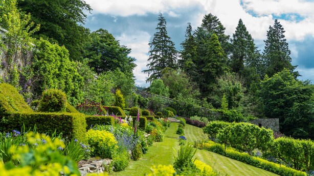 A well-maintained garden with manicured hedges, a variety of flowering plants, and a stone wall. - The Lodge at The Yair - Riverside comfort in the Scottish Borders (By Galashiels)