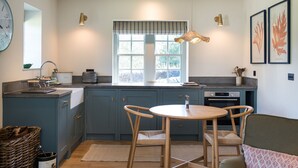 A modern kitchen with a large window, a dining table with chairs, and a hanging light fixture. - The Lodge at The Yair - Riverside comfort in the Scottish Borders (By Galashiels)