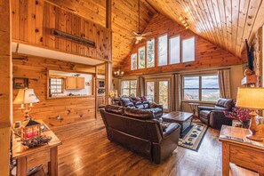 Een ruime houten blokhut met een grote woonruimte, compleet met leren banken, een eettafel en een kroonluchter.