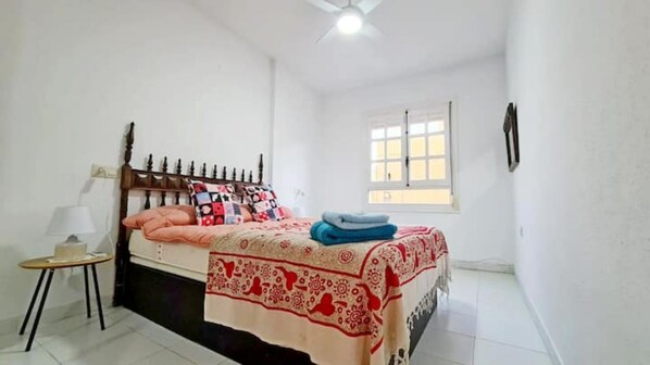 A bedroom with a bed, a bedside table, a lamp, a window, and a ceiling fan.