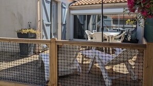 Un espace patio avec une table et des chaises, un parasol rouge et une vue sur un bâtiment doté d’un toit recouvert de tuiles.