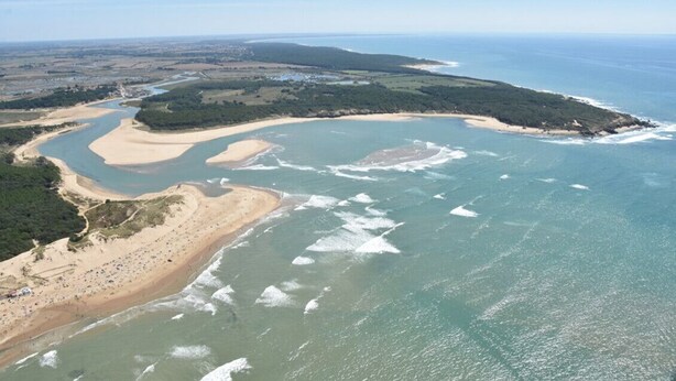 Vue aérienne d’une zone côtière comprenant une plage, une rivière et la végétation environnante.