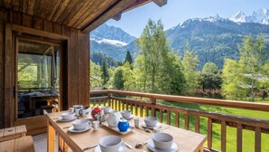 A wooden deck with a table set for breakfast, overlooking a mountainous landscape.