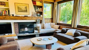 A cozy living room with a fireplace, comfortable seating, a coffee table, and a bookshelf.