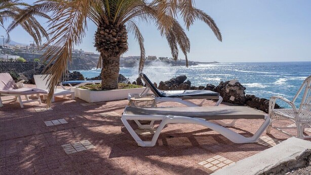 A beachside lounge area with white lounge chairs and a palm tree, overlooking the ocean. - Ocean front 3 bedroom apartment (Santiago del Teide)