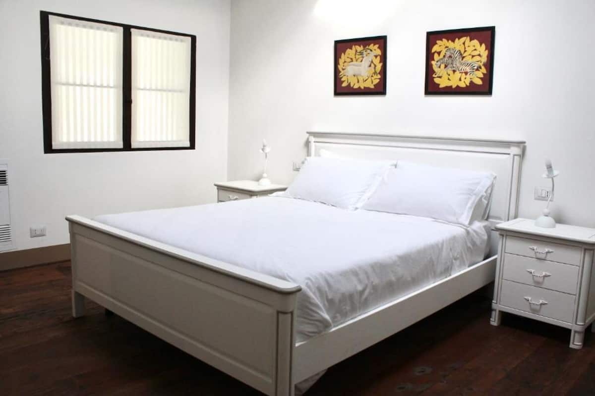 A white four-poster bed with white bedding, two bedside tables with lamps, and two framed artworks on the wall.