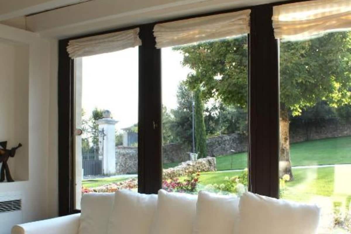 A white sofa with a wooden coffee table in a room with large windows, a view of a garden, and a ceiling with recessed lighting.