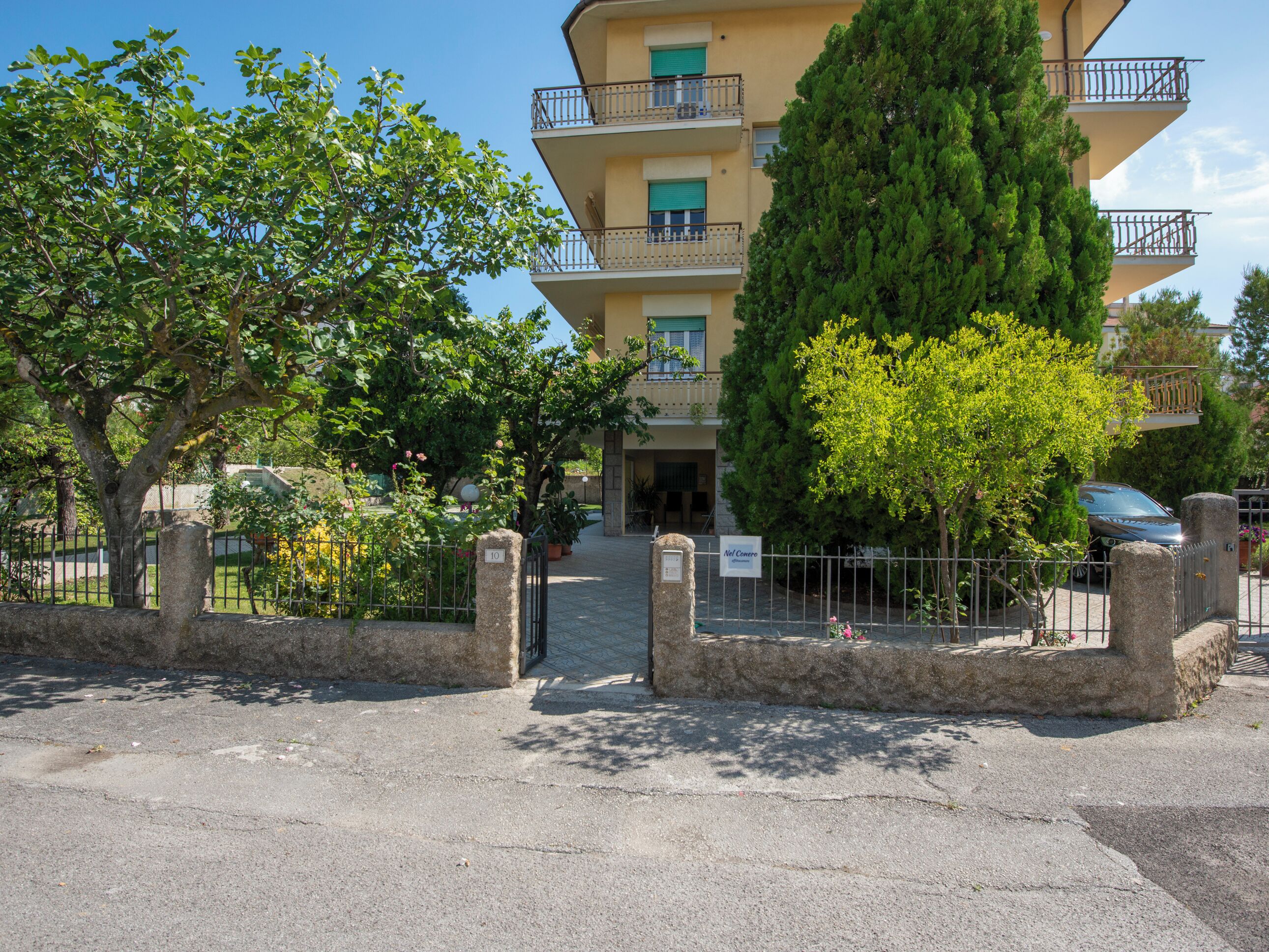 A multi-story building with balconies, surrounded by trees and a gated entrance.