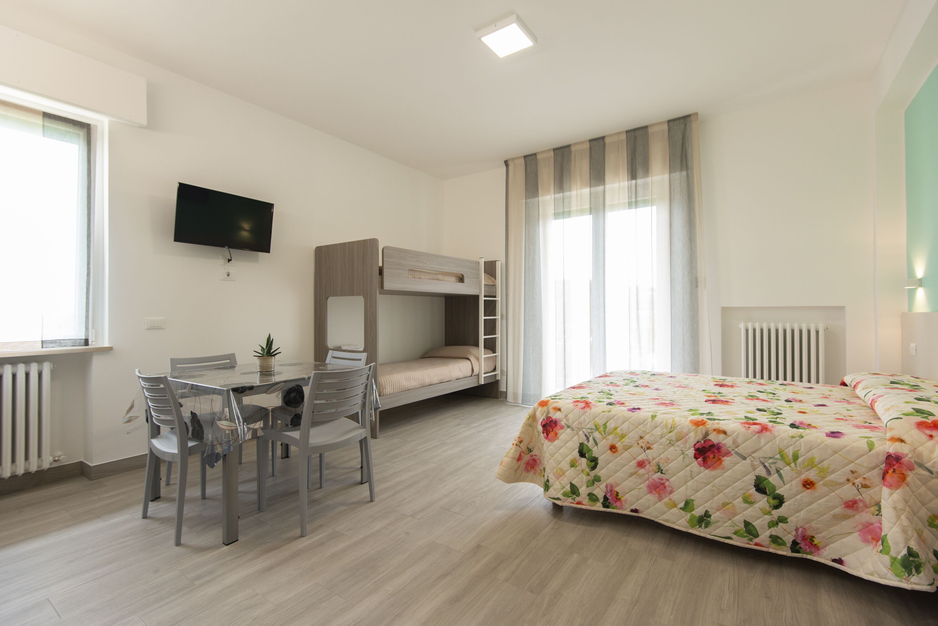Een slaapkamer met een stapelbed, een bureau met stoelen, een televisie en een bed met een bloemenquilt.