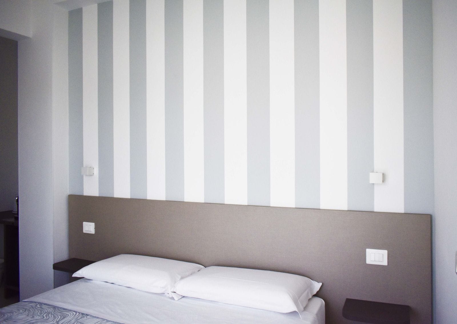 Una habitación de hotel con una cama, dos mesitas de noche y una pared con rayas verticales.